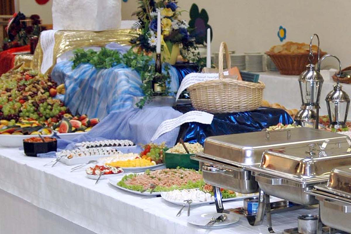 Ein dekorativ angerichteter Tisch eines Buffets mit Speisenwärmern und verschiedenen kalten Platten, Salaten, Brot und Obst